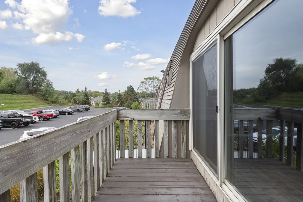 A wooden deck with a railing and a glass door leading to a house.