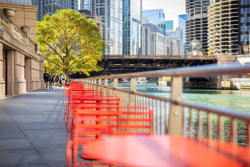 a row of red tables and chairs next to the river in a city at Columbus Plaza, Chicago, IL, 60601