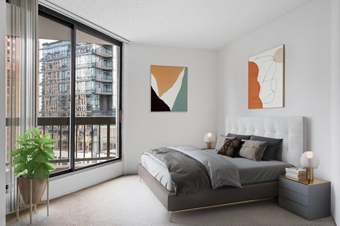 a bedroom with a large window and a bed with grey pillows and pillows
