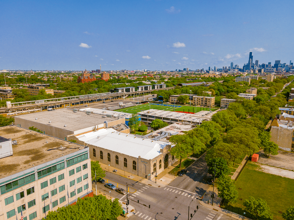 A cityscape with a mix of modern and older buildings, a large open area with trees, and a clear sky.