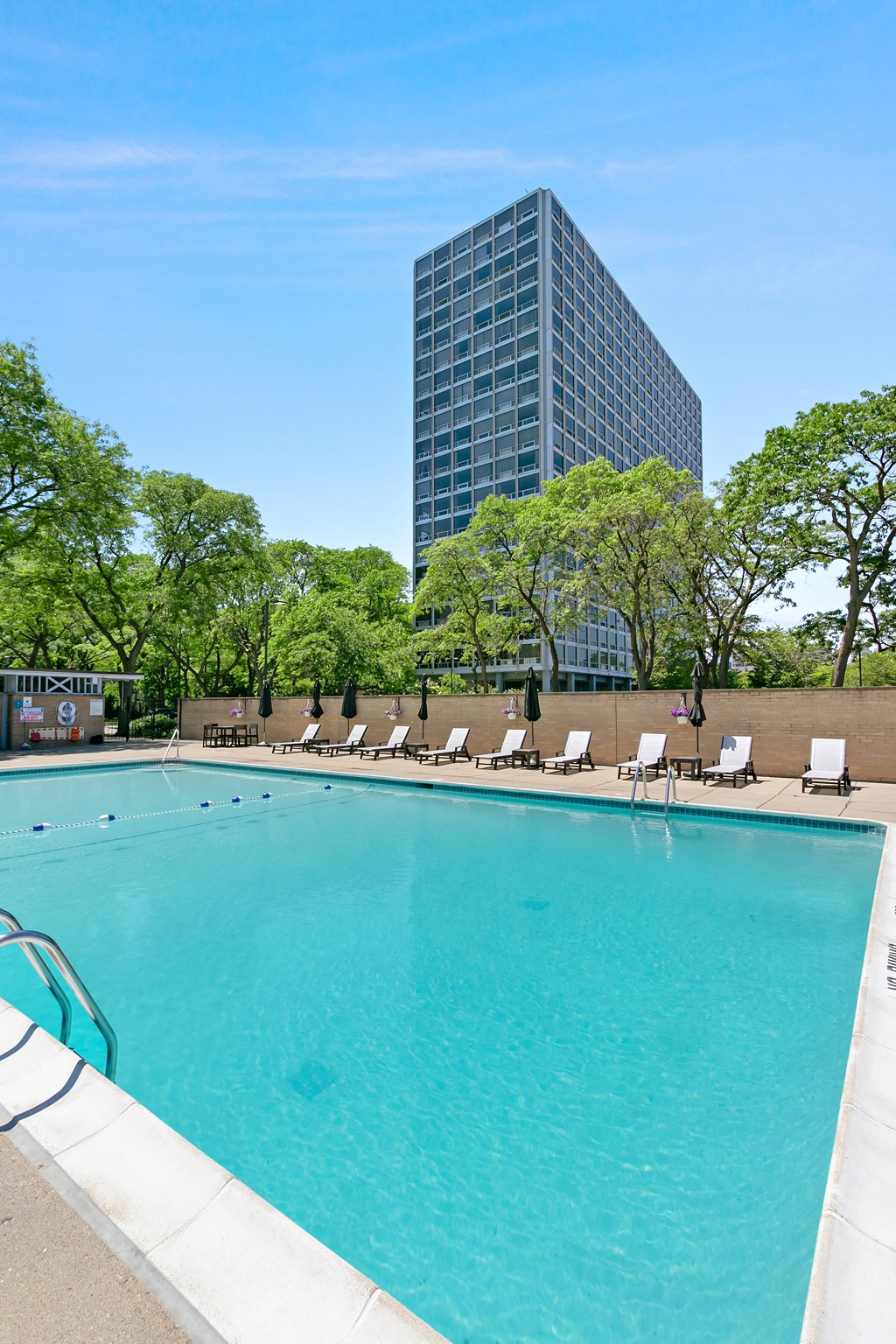 A swimming pool surrounded by trees and chairs with a building in the background at The Pavilion, Detroit, MI, 48207