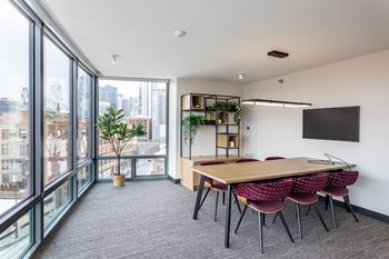 A conference room with a long table and chairs, a TV on the wall, and a view of the city outside the windows at Kingsbury Plaza Apartments, Chicago 60654