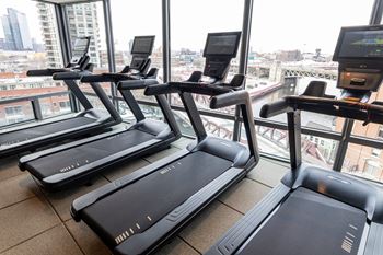 Three treadmills are lined up in a row in a gym with a city view at Kingsbury Plaza Apartments, Chicago
