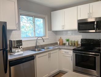 Cedarvale Elite one bedroom kitchen with stainless steel microwave, oven, dishwasher, and fridge, with elegant white cabinetry. 