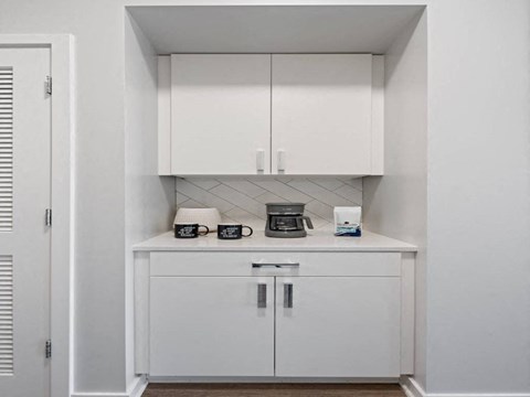 A white cabinet with a coffee maker and glasses on top.