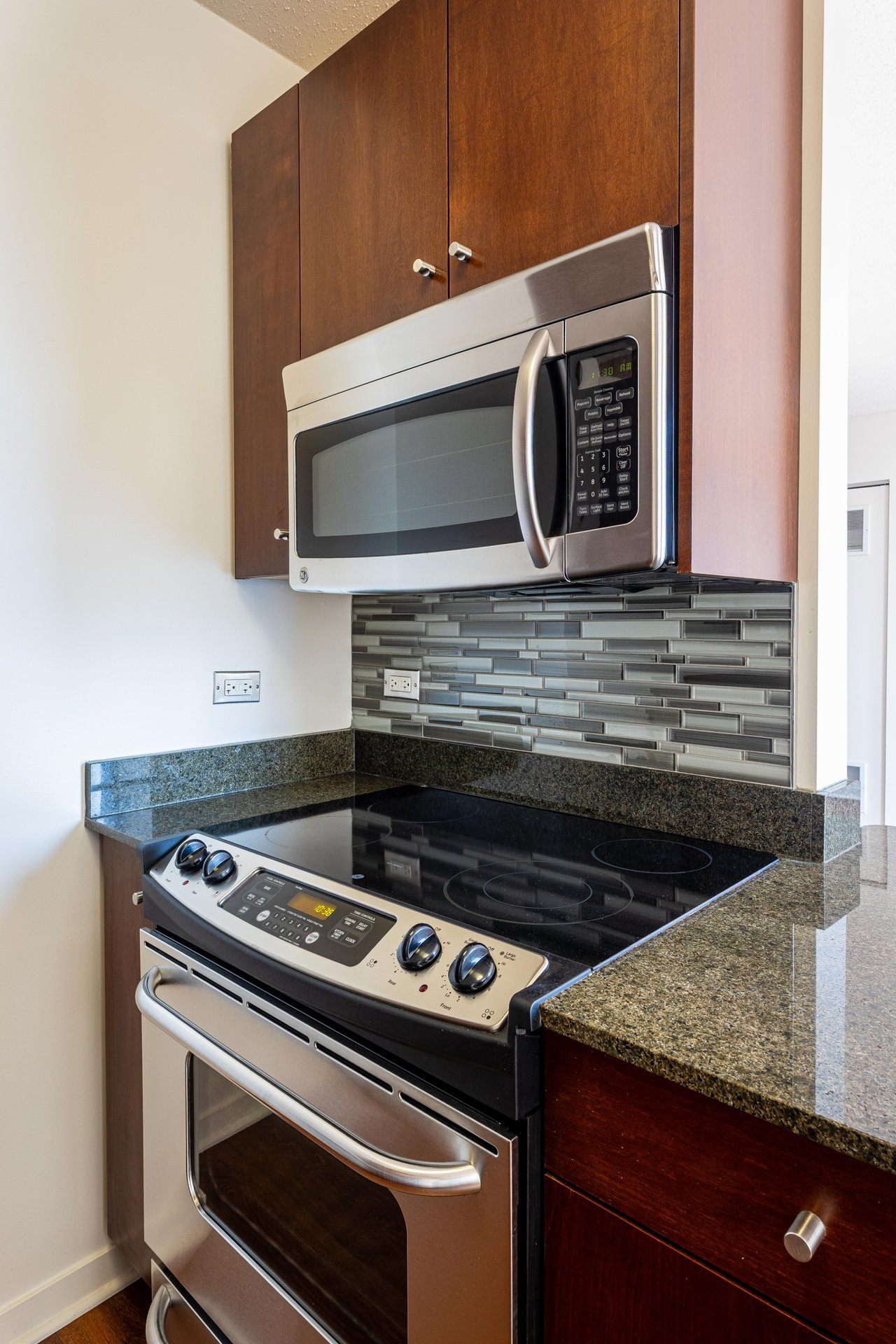 A modern kitchen with a stainless steel oven and microwave above a granite countertop.