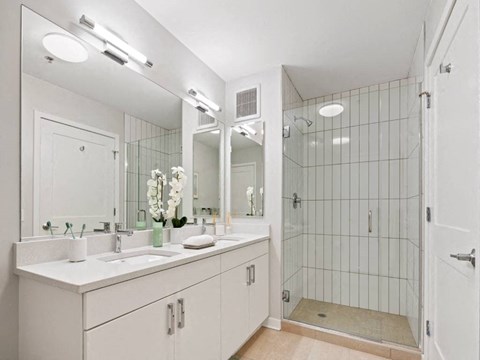 A white bathroom with a sink, mirror, and shower.