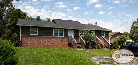 A house with a brick wall and a grey roof with a Universal Living logo in the corner.