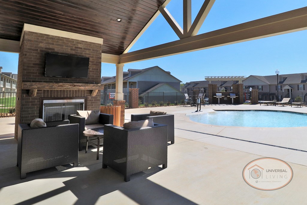 A poolside patio with fireplace, flat screen TV, and seating with a view of the pool and apartments in the background.