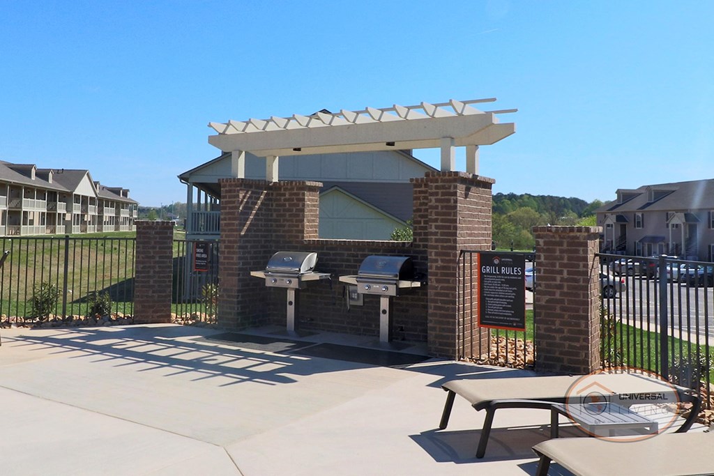 A grilling station with stainless steel grills, poolside lounge chairs, and a pool.
