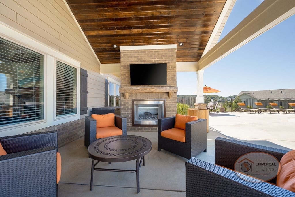 A poolside patio with fireplace, flat screen TV, and seating with a view of the pool and apartments in the background.