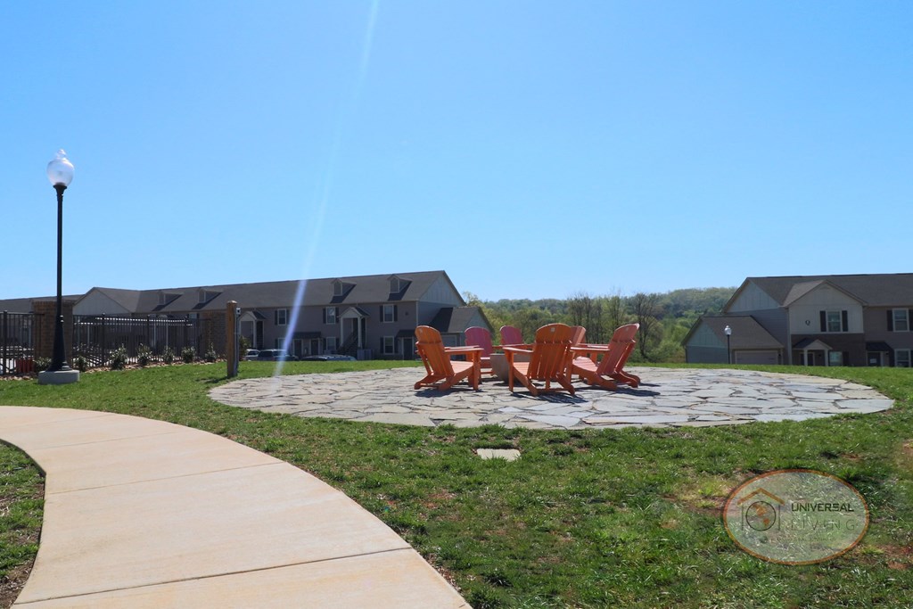 A fire pit on a stone patio with orange lounge chairs.