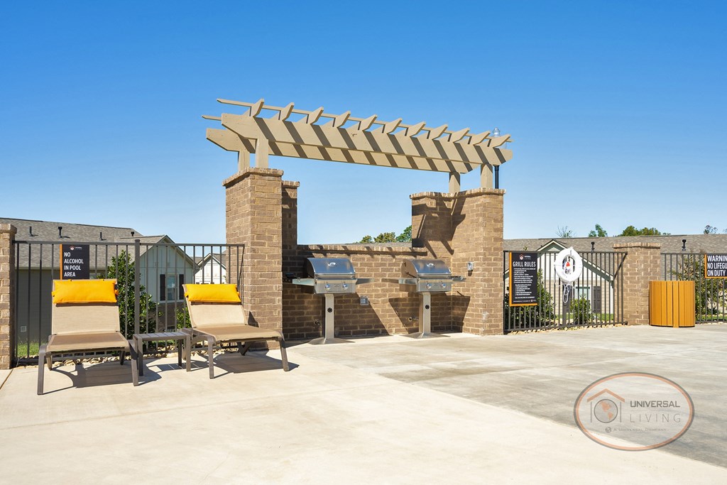 A grilling station with stainless steel grills, poolside lounge chairs, and a pool.