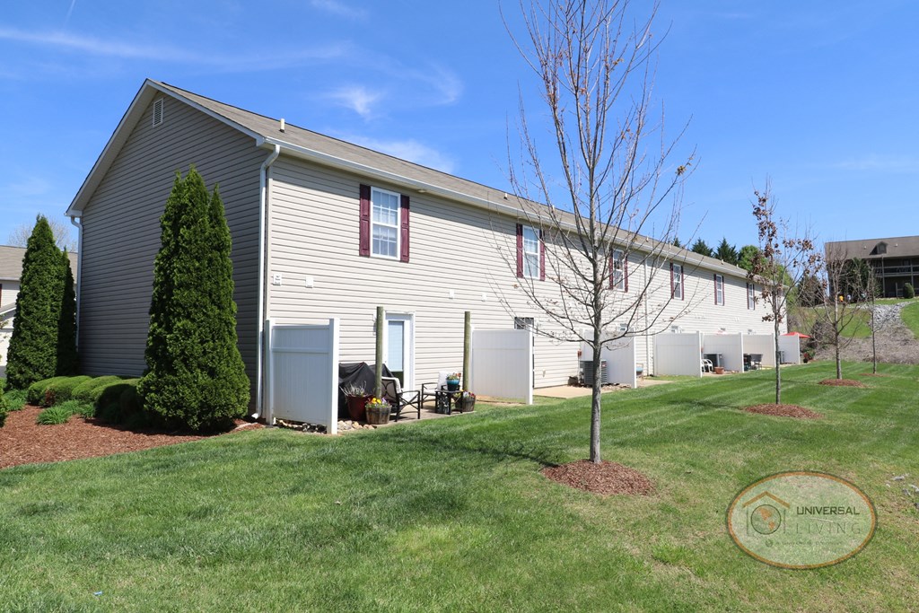 A large tan and white apartment home with maroon shutters, and a patio with privacy walls.