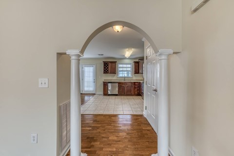 A hallway with a white archway leading to a kitchen.