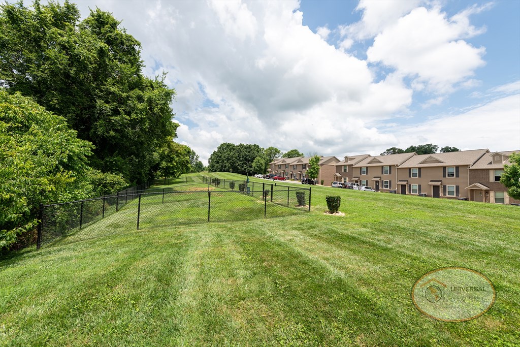 A fenced in dog park with apartment buildings in the background.