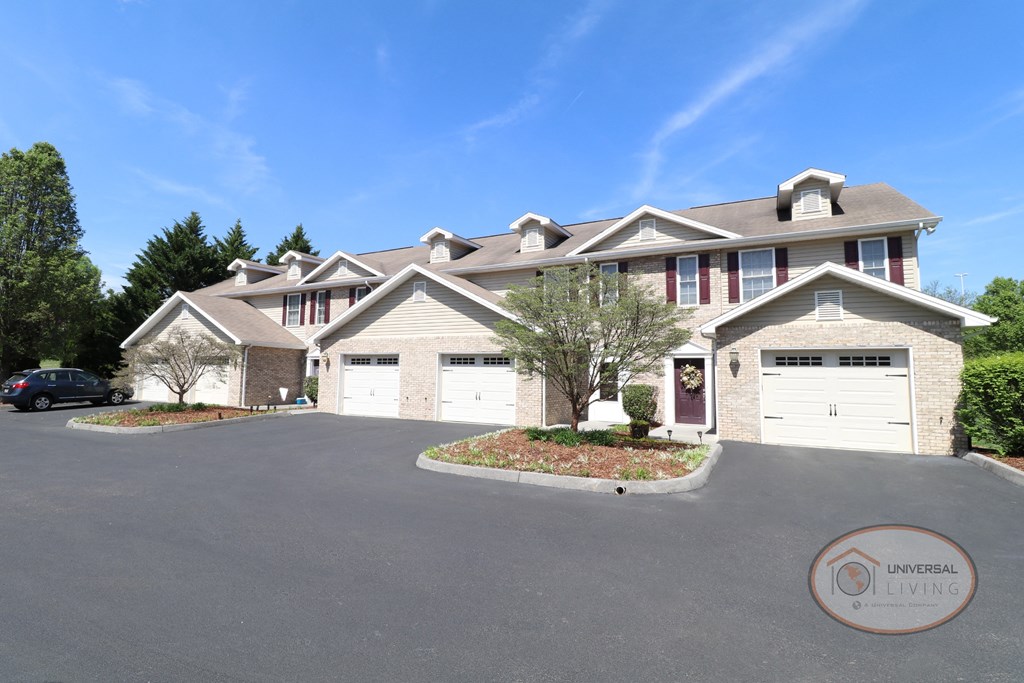 A large tan and white apartment home with maroon doors and shutters and garages.