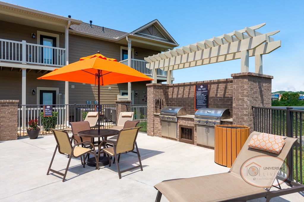 A grill station with two stainless steel grills against a brick enclosure surrounded by tables with umbrellas, and lounge seating.