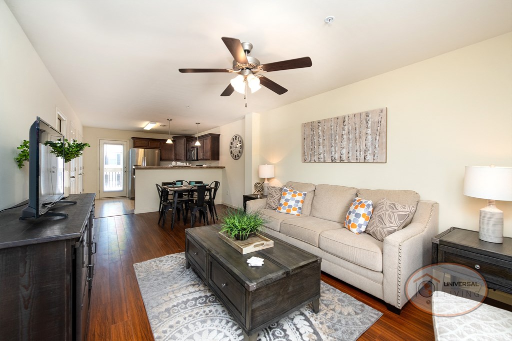 Living area with white walls, hardwood vinyl flooring, and a large kitchen.