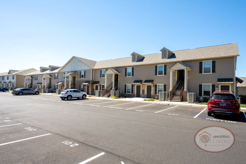 A tan, two story apartment building with ample parking.