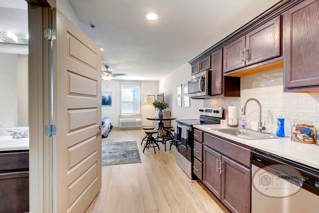 A studio apartment kitchen with dark cabinets and hardwood style vinyl flooring.