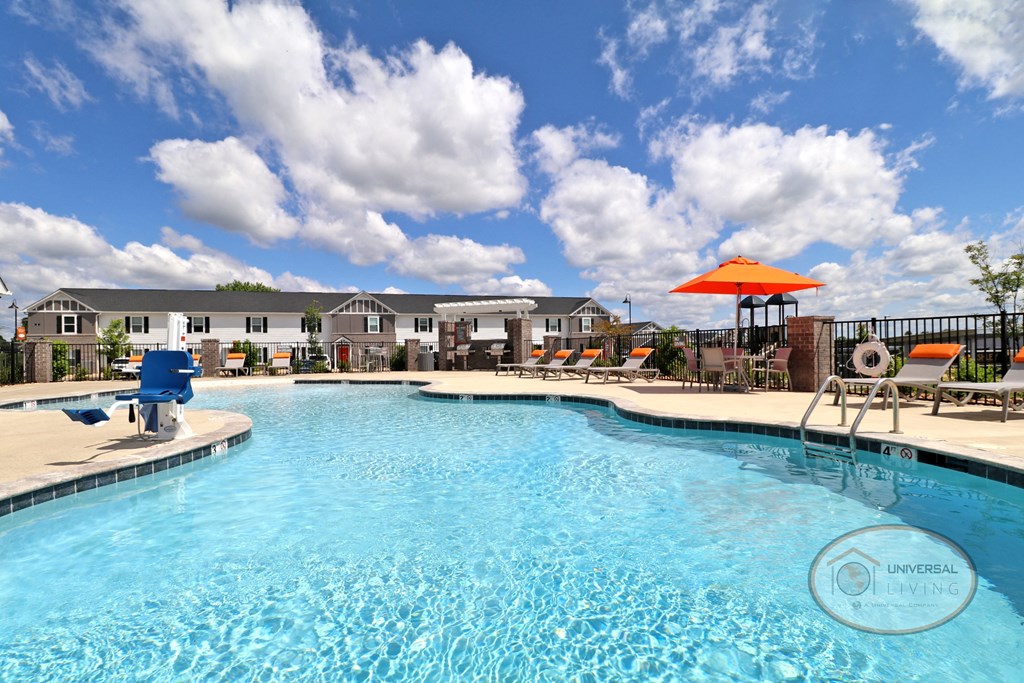 A view of the pool with white and gray apartment building in background and orange patio furniture.