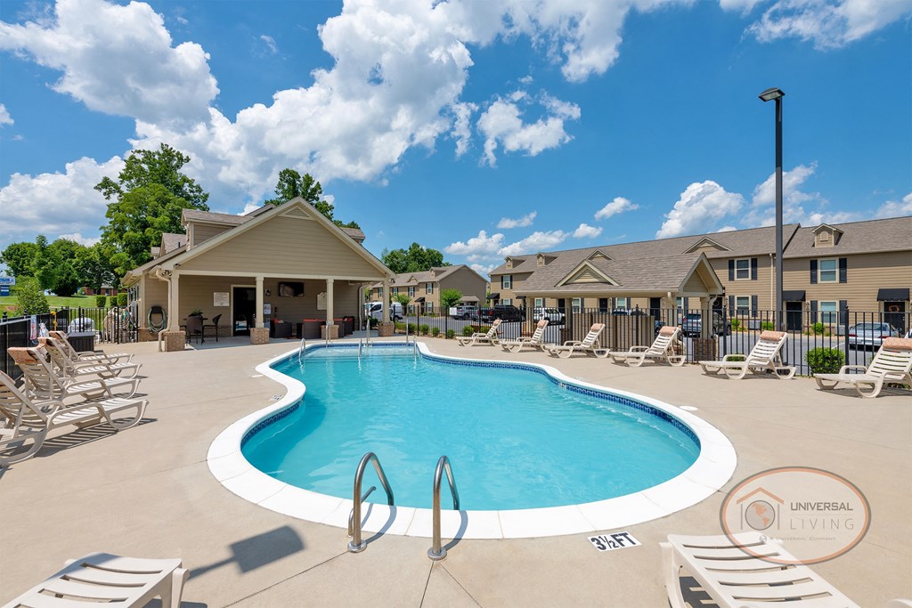 A pool with lounge chairs, a clubhouse and apartment buildings in the background.