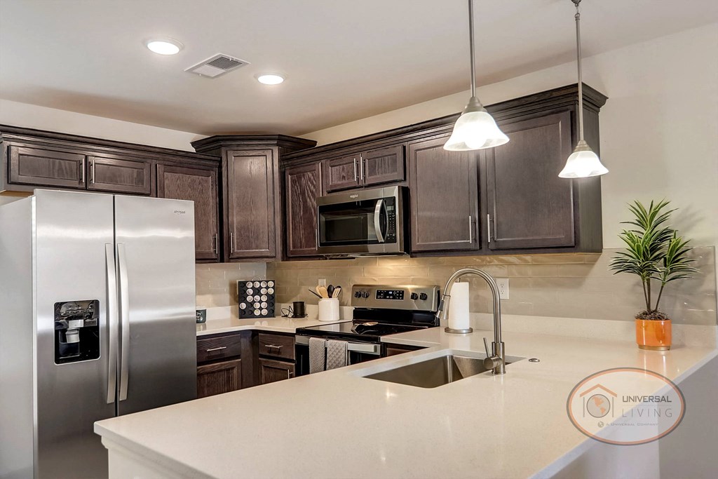 A kitchen with stainless steel appliances, dark cabinets, and a white counter tops.