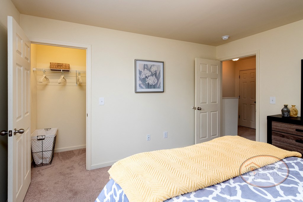 A bedroom with white walls, carpet, and a walk in closet.