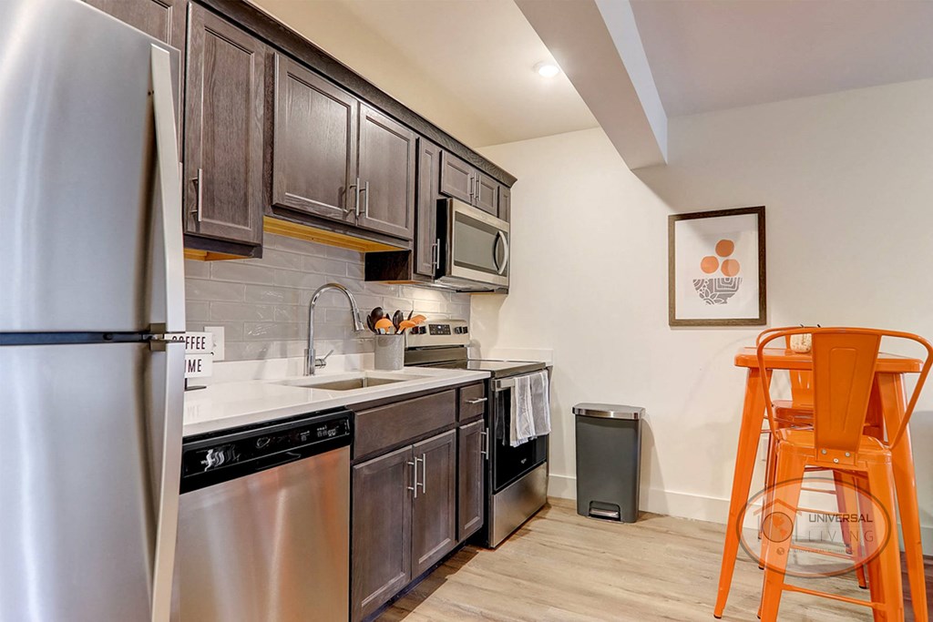 The Hub at Mountcastle Johnson City, TN- Kitchen A kitchen with stainless steel appliances and wooden cabinets with an orange table and chairs.