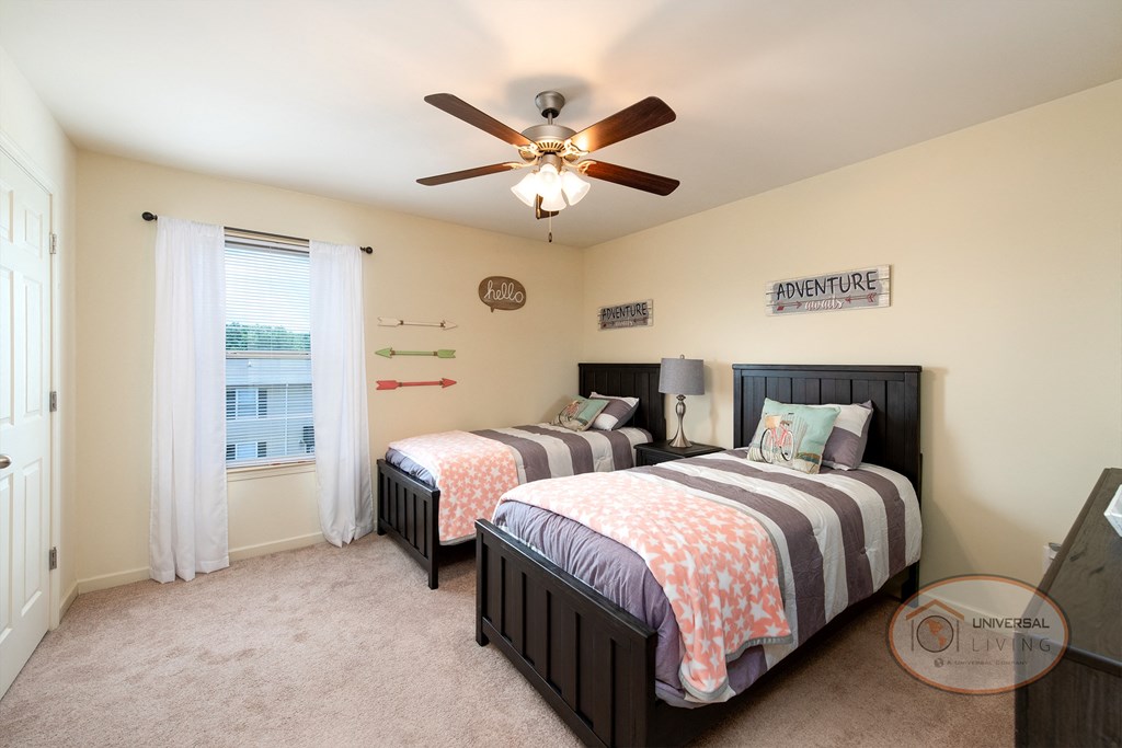 A bedroom with two twin beds, carpet, white walls, and a window.