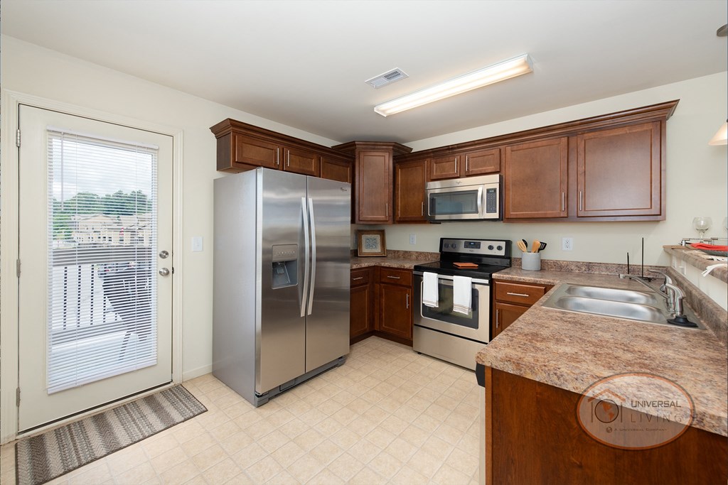 A kitchen with stainless steel appliances and wooden cabinets with tile flooring.
