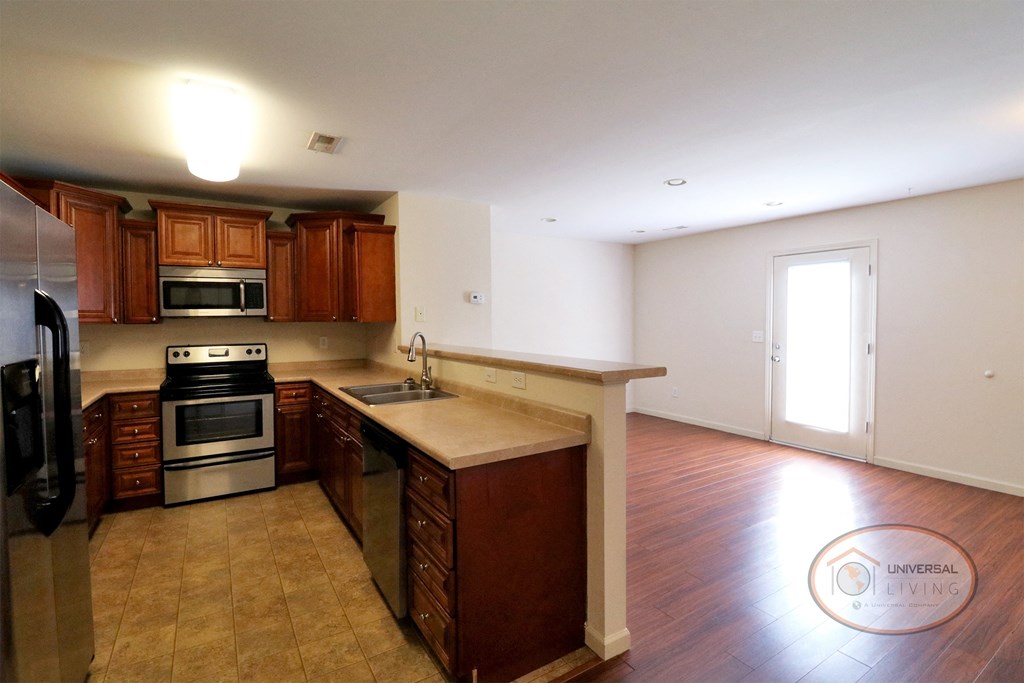 An empty kitchen with dark wood flooring and wooden cabinets.