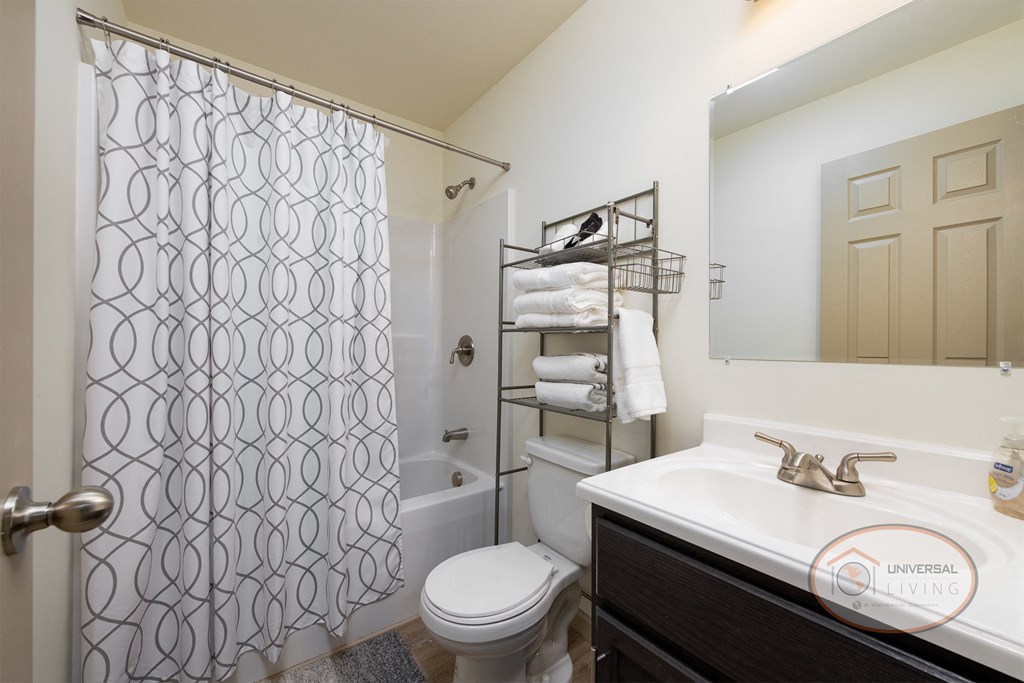 A bathroom with white walls, dark cabinets, and a shower, a sink, and a toilet.
