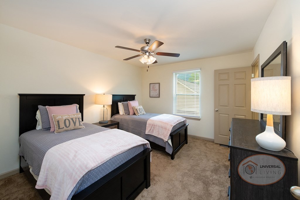 A bedroom with two twin beds, carpet, white walls, and a window.