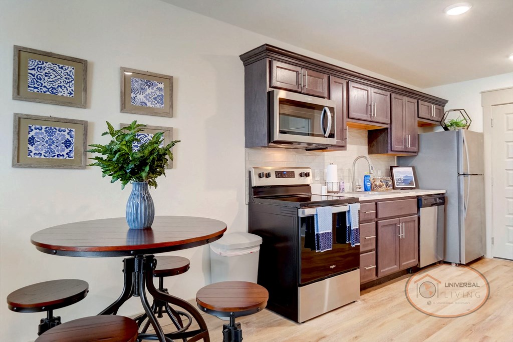 A studio apartment kitchen and dining area with white counters and dark cabinets.