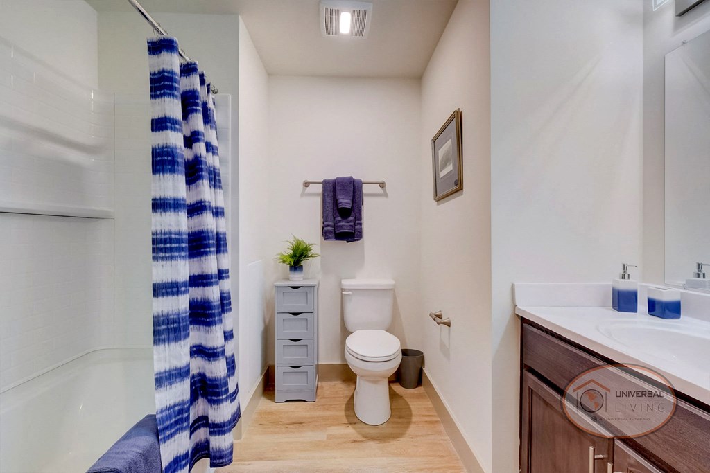 A bathroom with white counters and dark cabinets with toilet, sink, and shower.