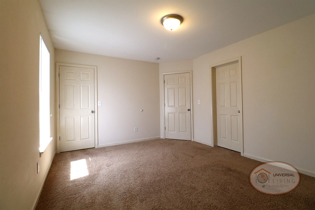 An empty bedroom with tan carpet, white walls, a walk in closet and a bathroom.