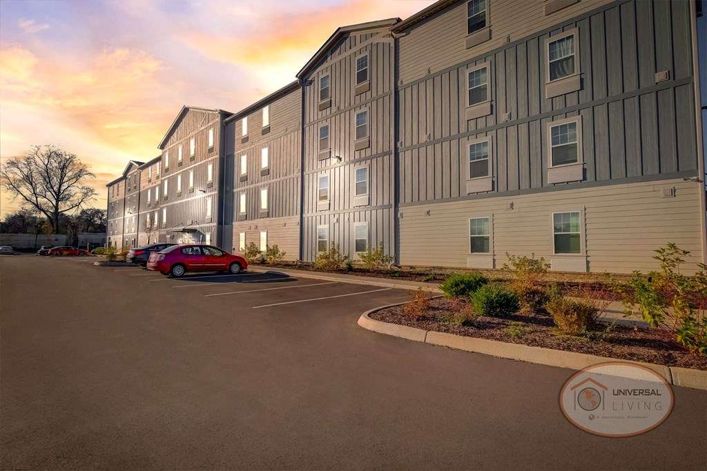 Exterior view of a grey and blue apartment home complex with ample parking at night.