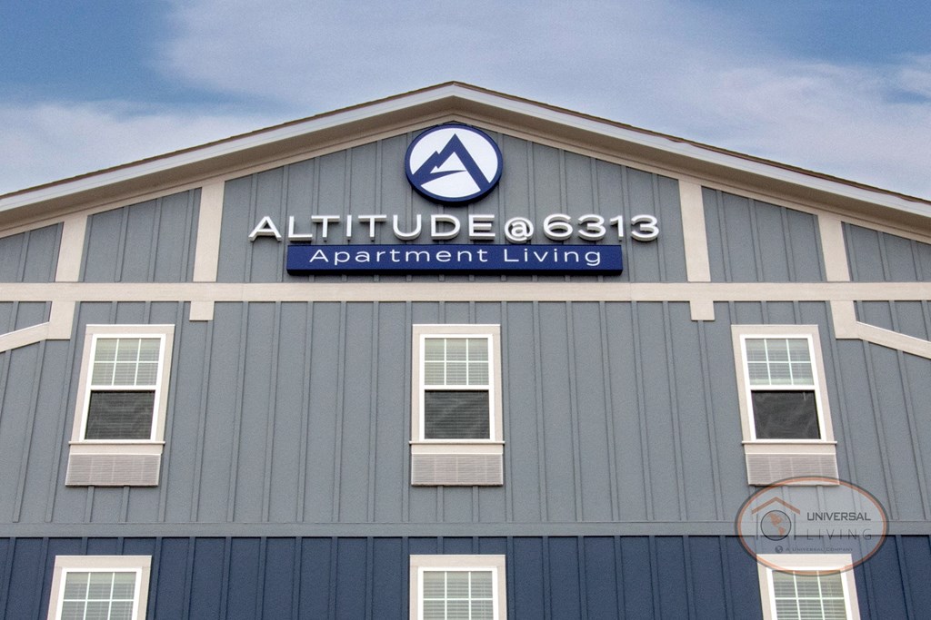 The front of a grey and blue apartment building that reads "Altitude @ 6313 Apartment Living"
