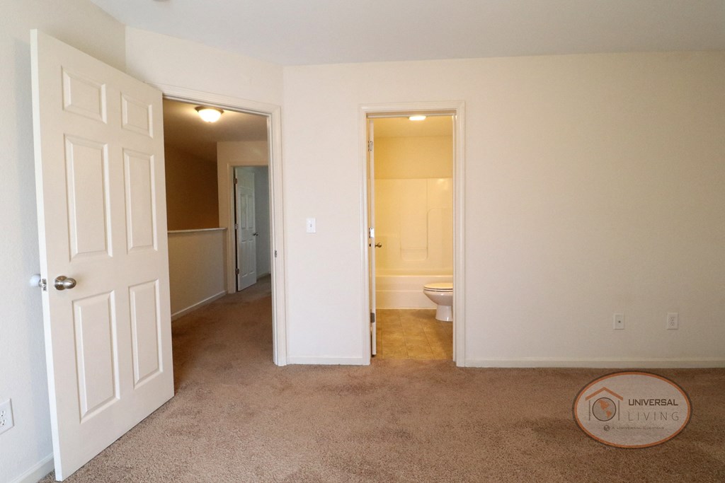 An empty bedroom with bathroom, white walls, and tan carpet.