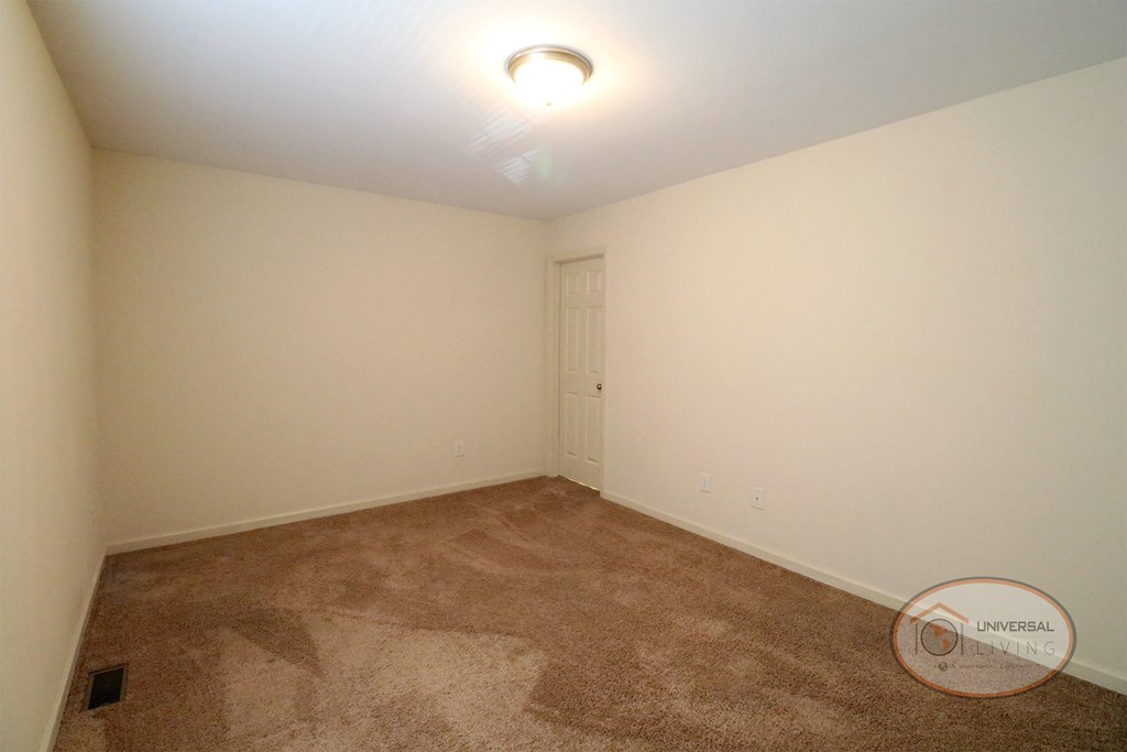 An empty bedroom with white walls and tan carpet.