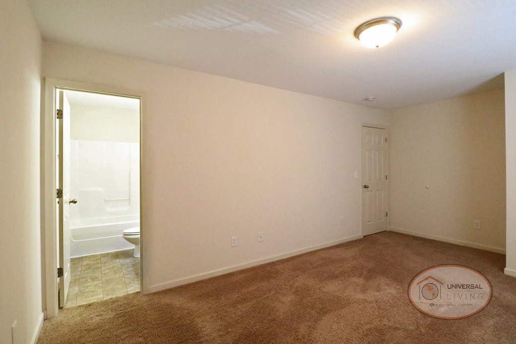 A bedroom with white walls, carpet, and a bathroom.
