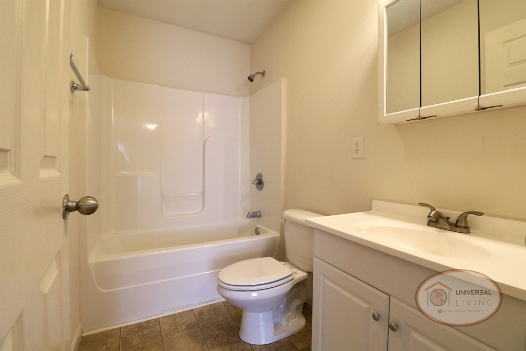 A full bathroom with shower over the tub, sink, cabinet, and toilet.