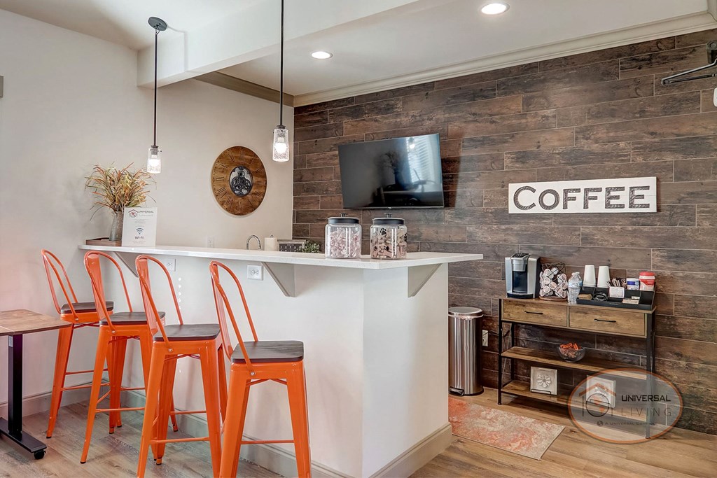 Coffee Bar against a stone backdrop with white island, orange barstools, and a flat screen TV.