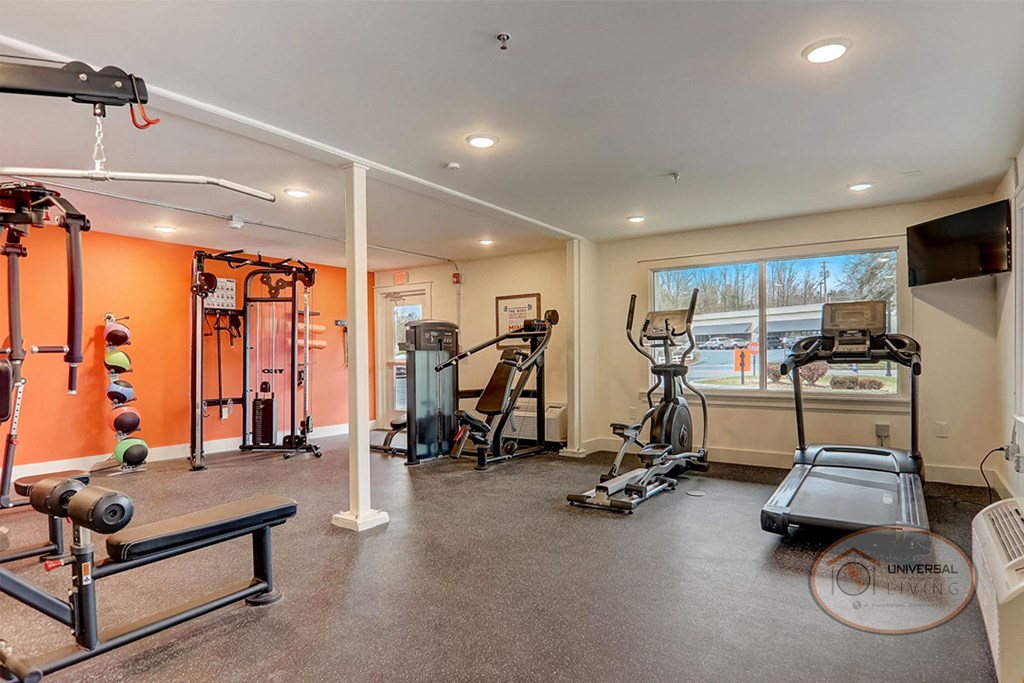 The Hub at Mountcastle Johnson City, TN - Fitness Center A fitness center with a wall of mirror and an orange accent wall, featuring weight training equipment and cardio equipment.