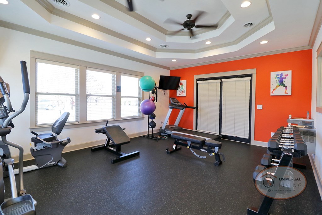 A fitness center with a wall of mirror and an orange accent wall, featuring weight training equipment and cardio equipment.