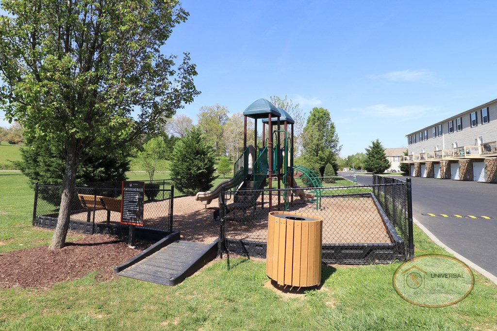 A fenced in playground with slide and jungle gym in front of a row of apartment homes.