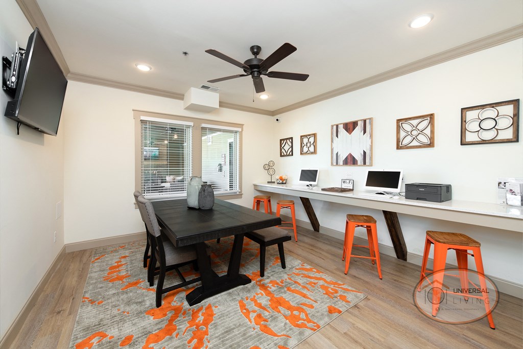 Business center with flat screen TV, lounge chairs, and a desk with computers and a printer.