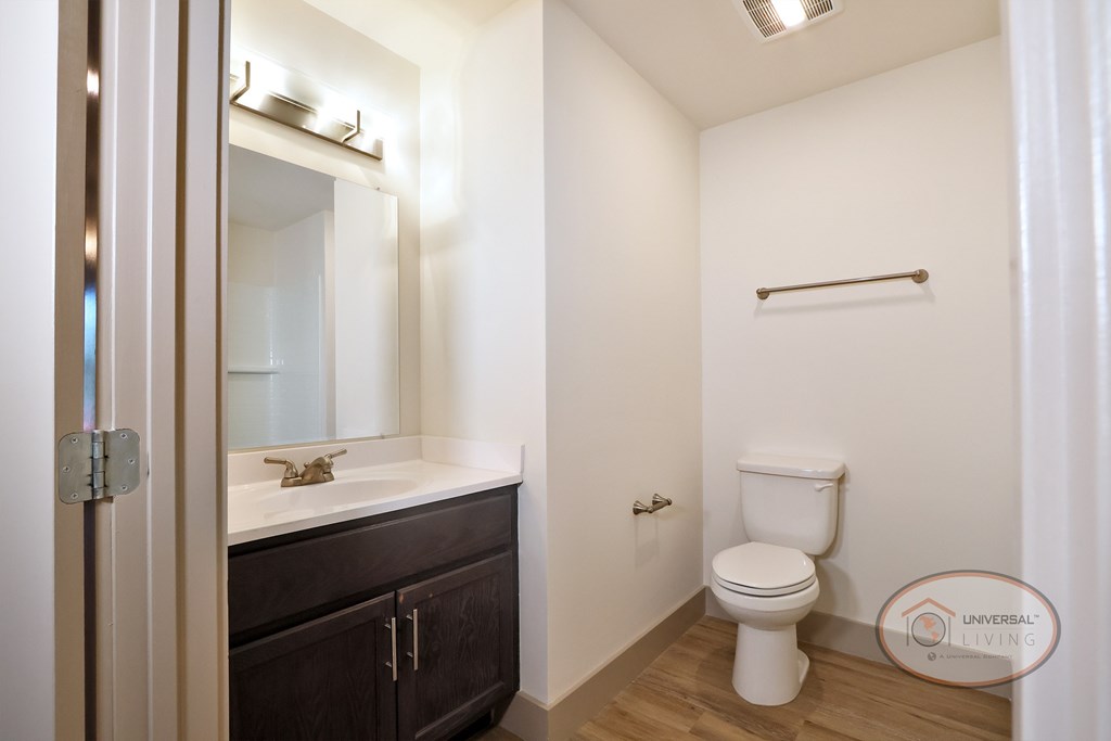 A bathroom with white walls, hardwood vinyl flooring, car cabinets and white countertops.